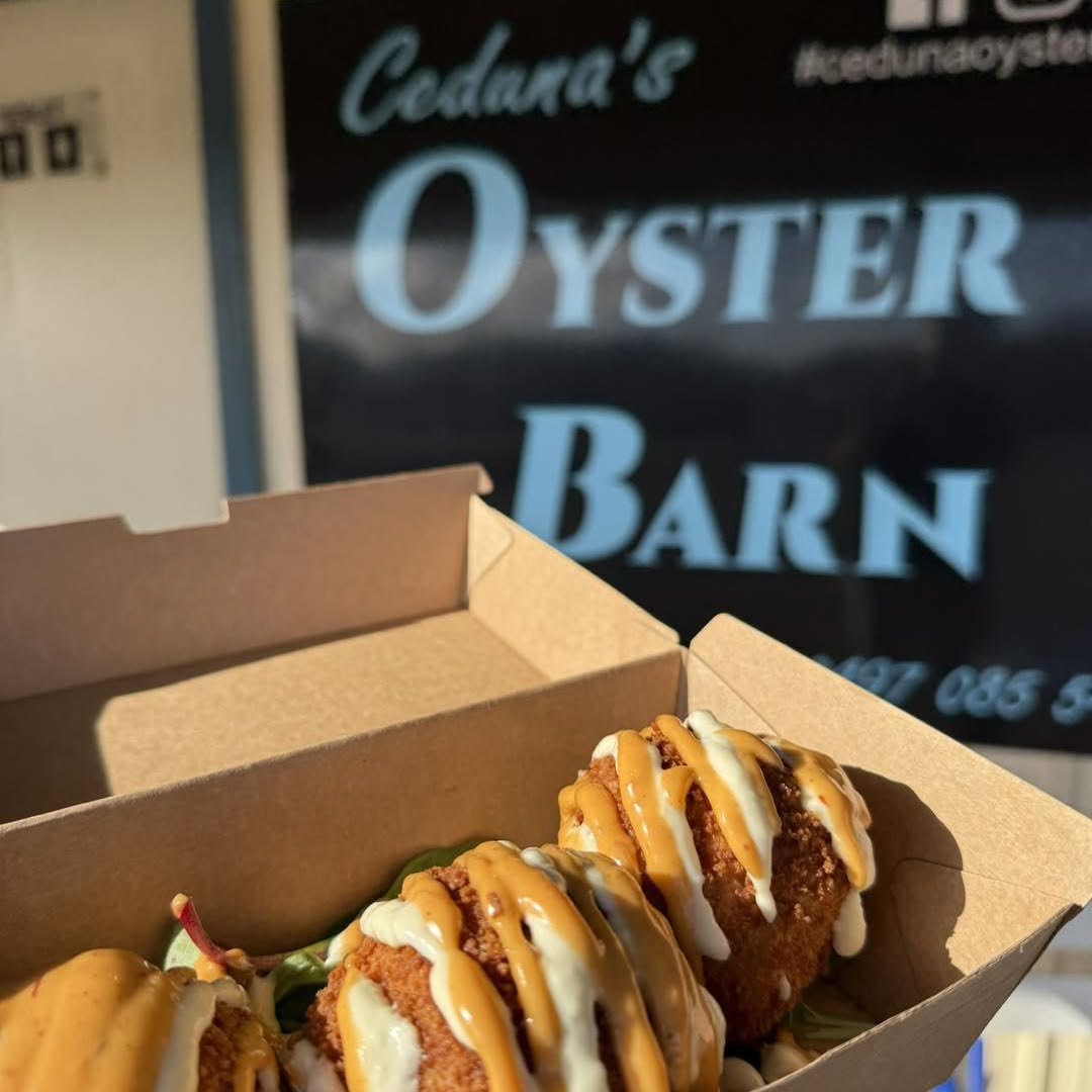 Crumbed oysters drizzled with two sauces in a takeaway box, the shopfront sign behind