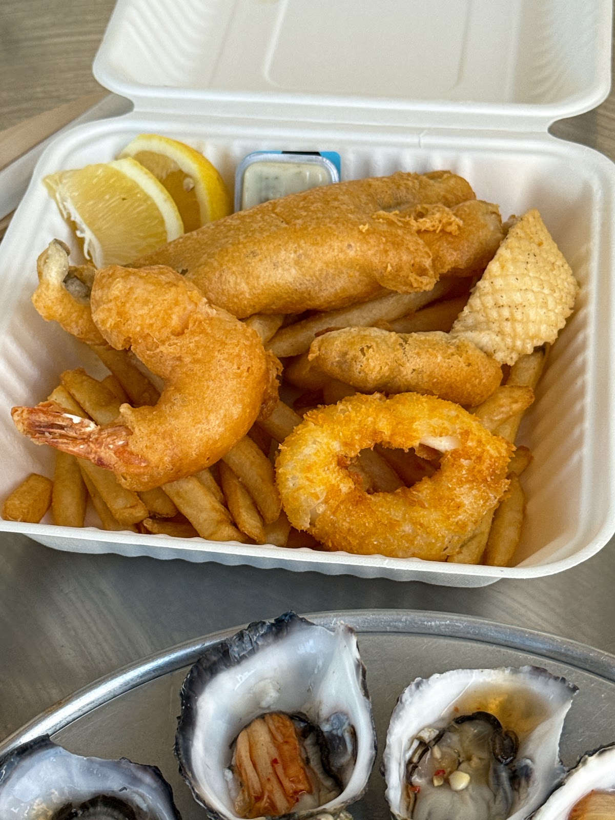 A box of fish and chips with a prawn, a squid ring and a potato scallop